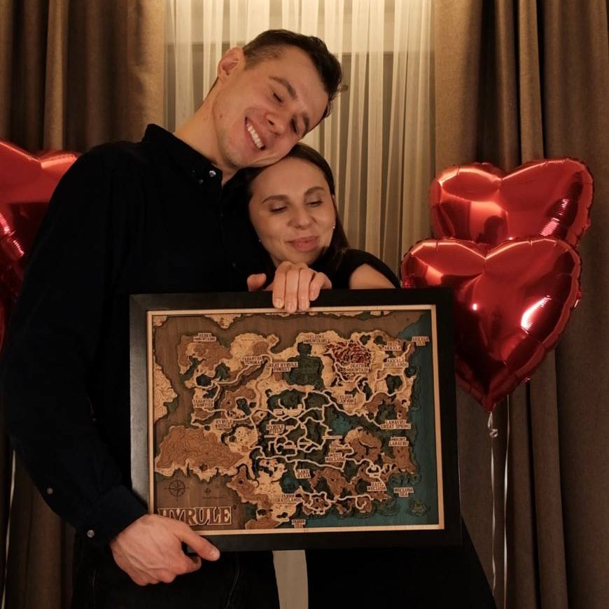 Two people holding a framed map with red heart balloons in the background.